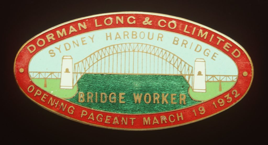 A Sydney Harbour Bridge workers entry badge. The brass badge is oval in shape and has been enamelled in red, blue, green and white. The badge features an image of Sydney Harbour Bridge. The pin on the back of the badge is missing. Text above and below the image of the bridge reads 'SYDNEY HARBOUR BRIDGE / BRIDGE WORKER'. Text in the red border around the image of the bridge reads 'DORMAN LONG & CO LIMITED / OPENING PAGEANT MARCH 19 1932'. Engraved on the back of the badge 'AMOR / SYDNEY'.
